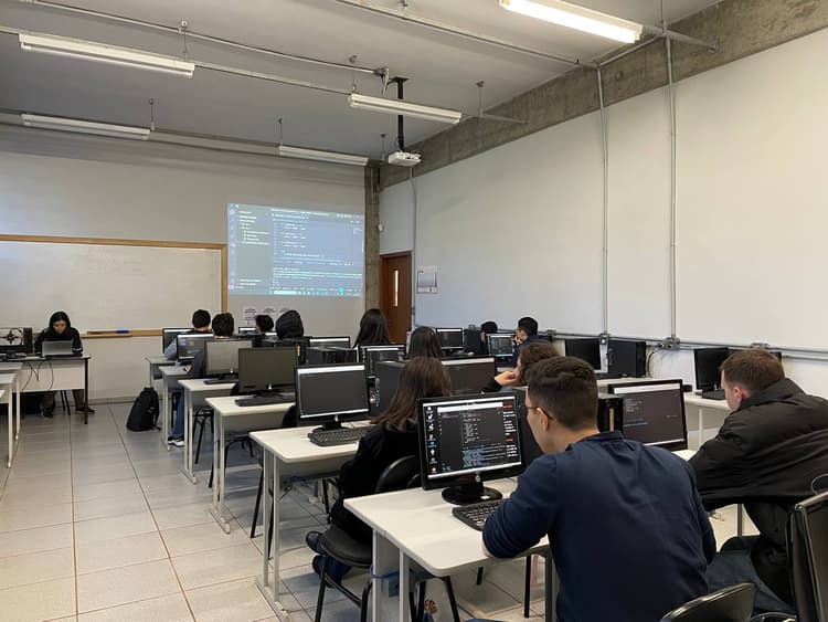 Pessoas sentadas a frente de computadores em uma sala de aula